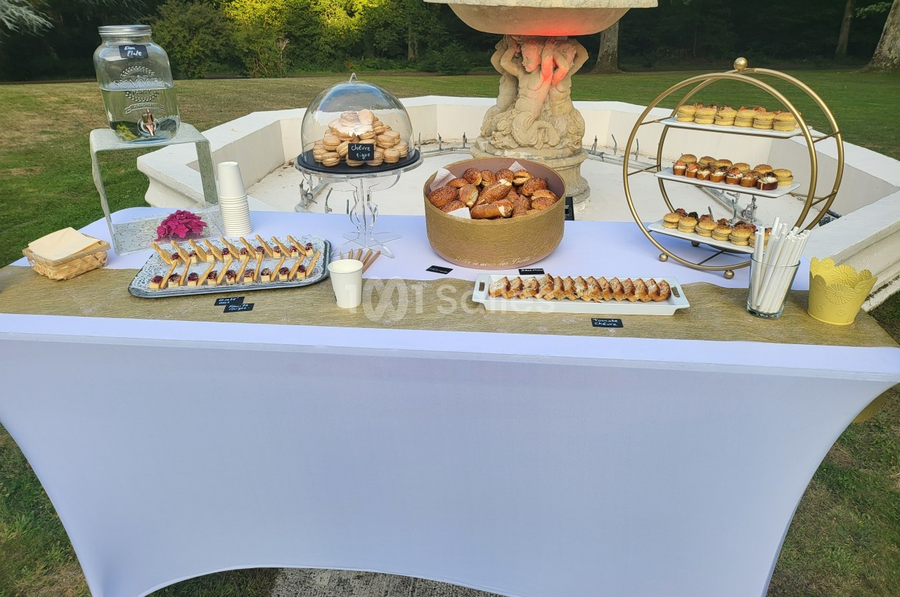 Table de buffet en extérieur avec viennoiseries, pâtisseries, distributeur d'eau et vaisselle jetable.