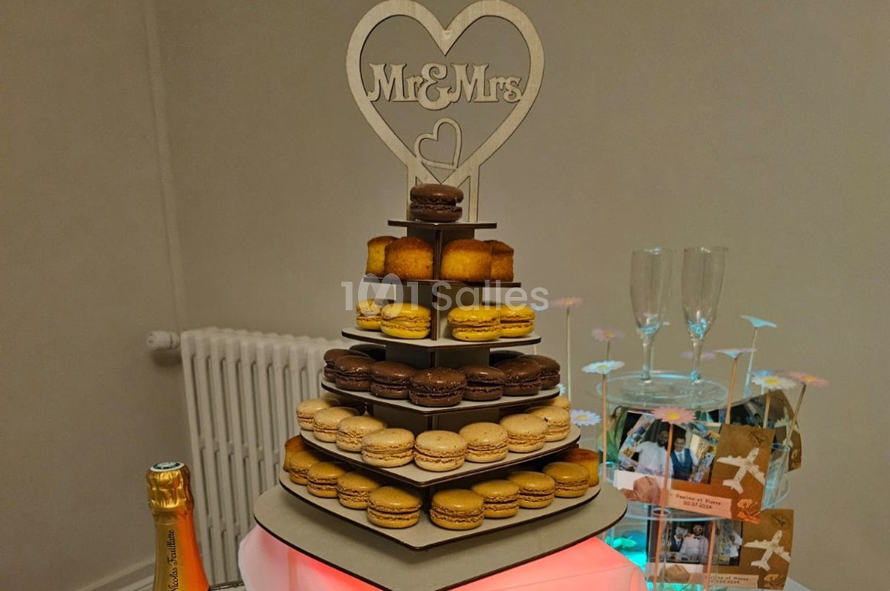 Tour de macarons et petits gâteaux sur un présentoir décoré d'un cœur ’Mr & Mrs’, entourée d'éléments de fête.