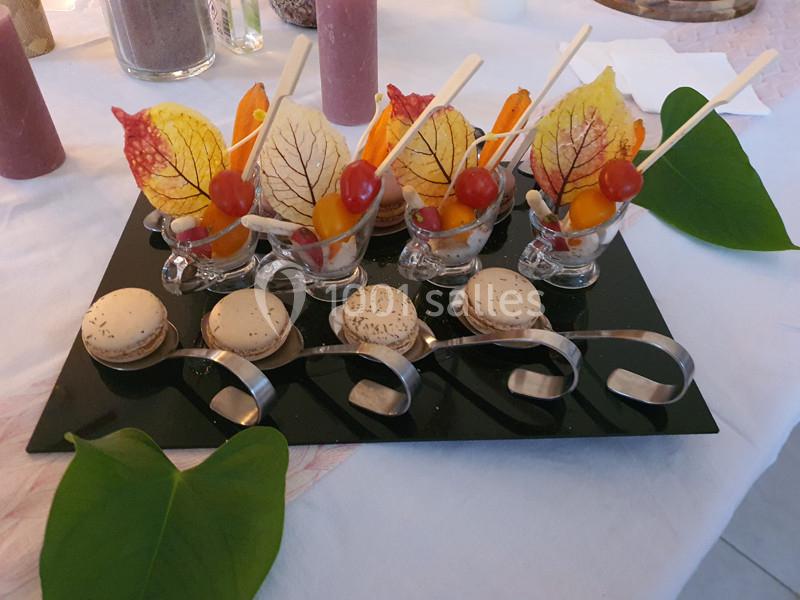 Plateau de verrines décorées de feuilles colorées et de brochettes, accompagné de macarons sur une table blanche.