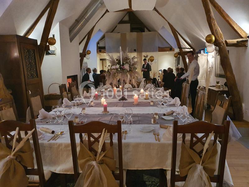 Salle de réception décorée avec des tables dressées, des bougies allumées et des invités en arrière-plan.