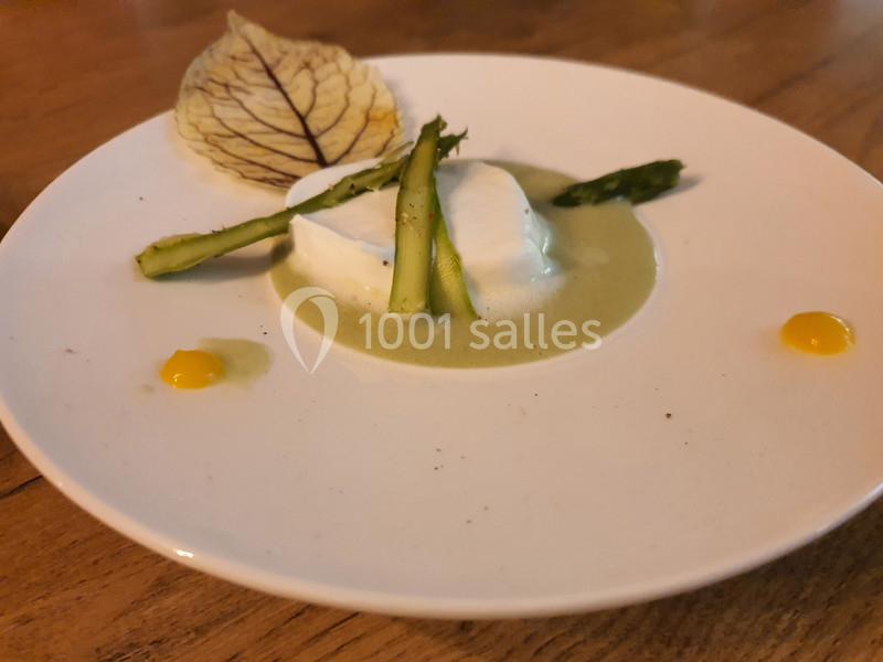 Assiette avec une mousse blanche, asperges, sauce verte, points de purée jaune et une feuille décorative.