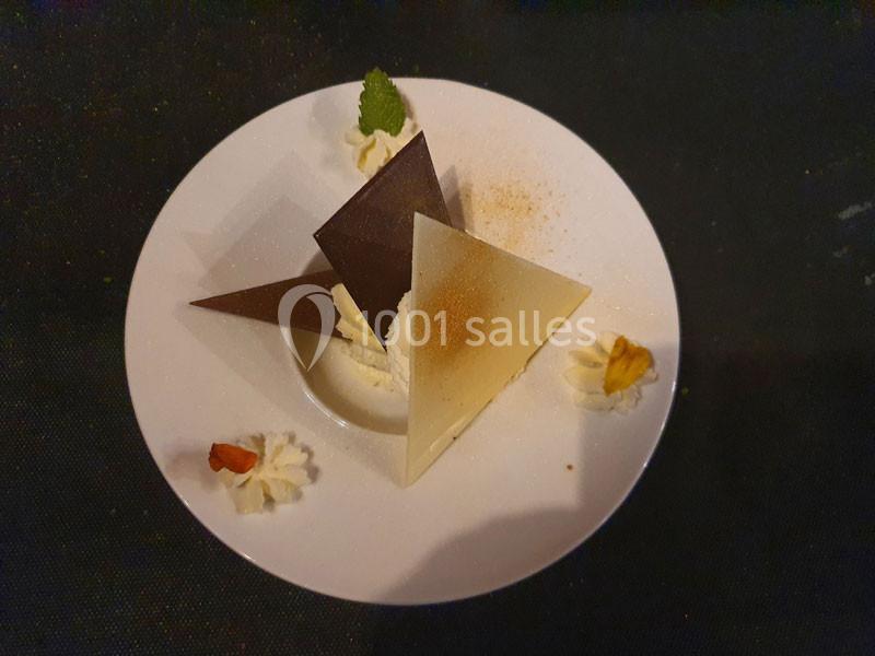 Assiette de dessert avec des triangles de chocolat noir et blanc, crème fouettée et décorations de feuilles et noix.