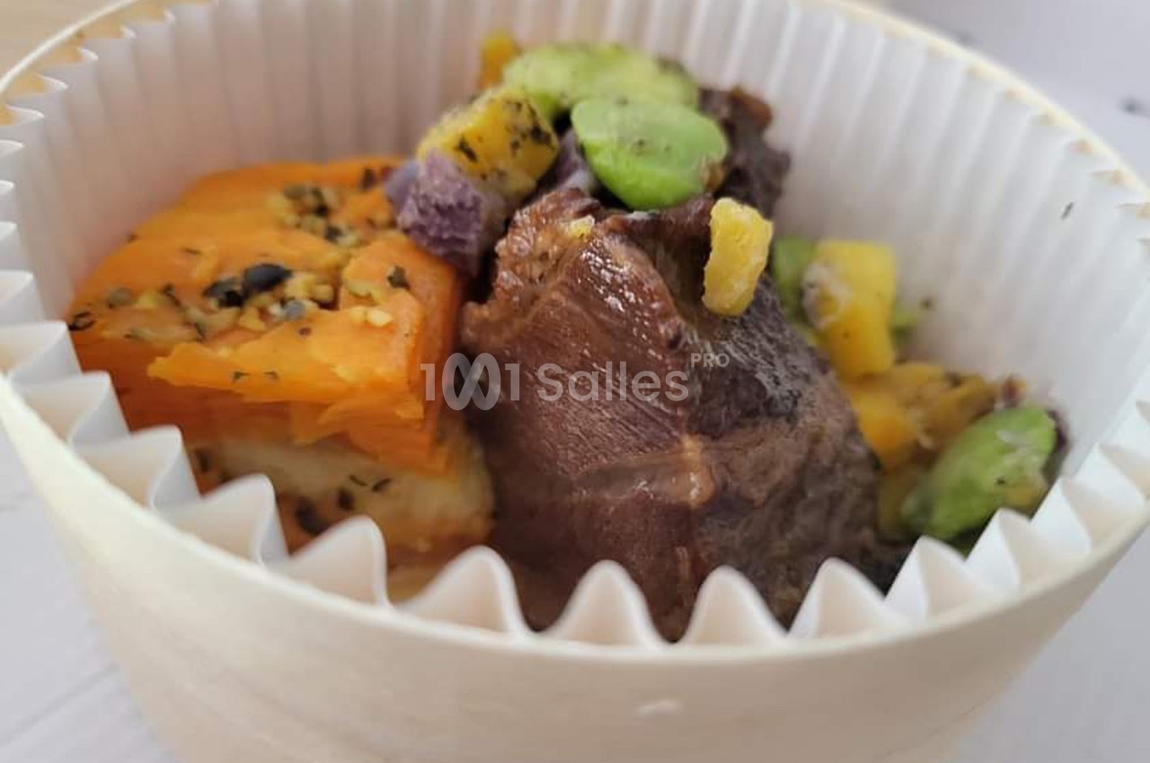 Plat servi dans un contenant en carton, composé de viande, patate douce, fèves et morceaux de légumes colorés.