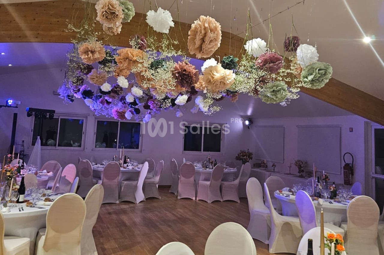 Salle de réception décorée avec des tables dressées et des fleurs suspendues au plafond.