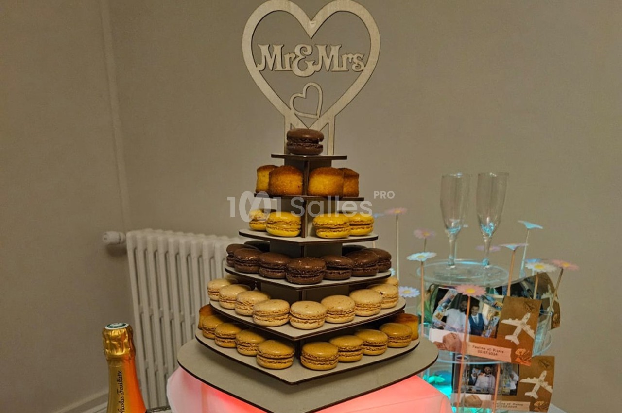 Tour de macarons et petits gâteaux sur un présentoir décoré d'un cœur ’Mr & Mrs’, entourée d'éléments de fête.