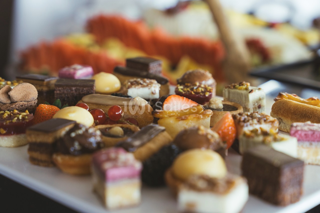 Assortiment de petits desserts variés disposés sur un plateau, avec des fruits et des pâtisseries colorées.