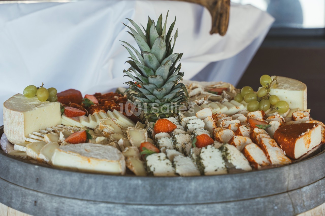 Plateau de fromages variés avec des fruits frais, dont des raisins, des fraises et un ananas au centre.