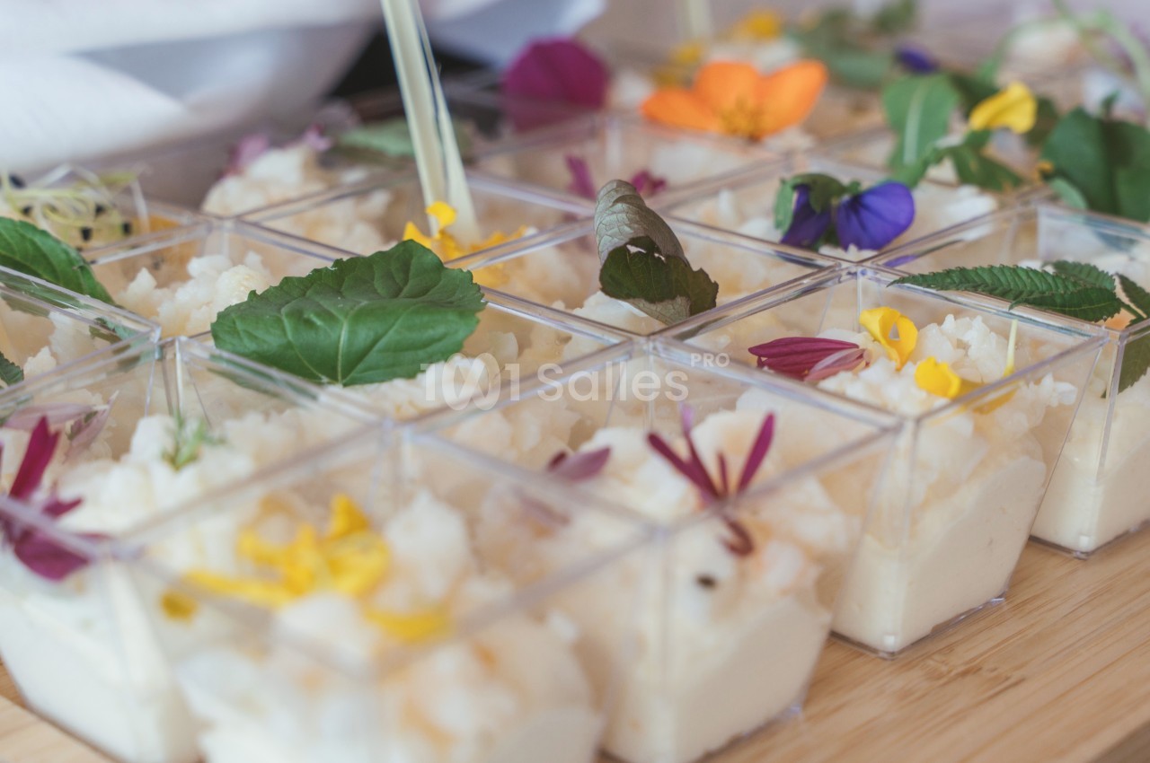 Petits verrines de mousse blanche décorées de fleurs comestibles colorées sur une table en bois.
