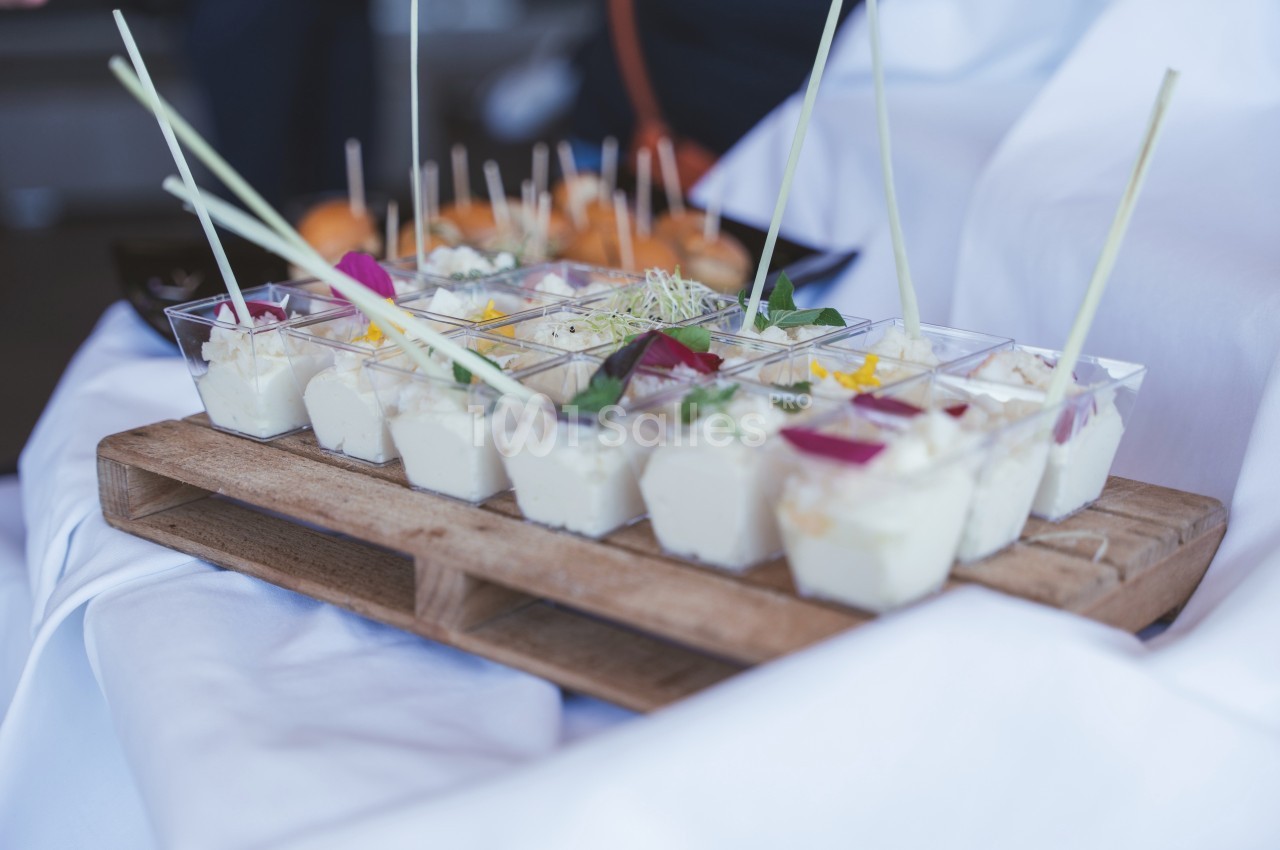 Plateau en bois avec verrines de mousse blanche garnies de fleurs et herbes, présenté sur une nappe blanche.