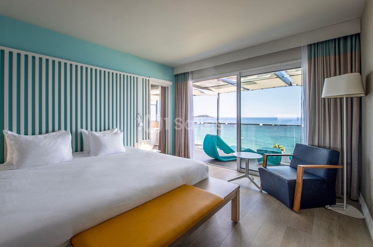 Chambre lumineuse avec lit double, mobilier moderne et vue sur la mer depuis une grande baie vitrée.