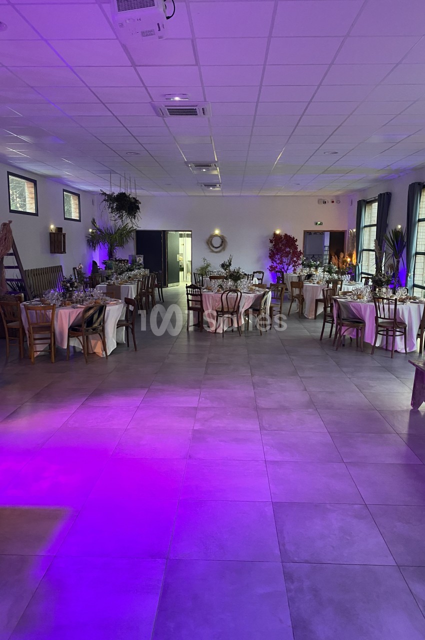 Salle de réception décorée avec des tables dressées, éclairage tamisé et ambiance lumineuse violette.