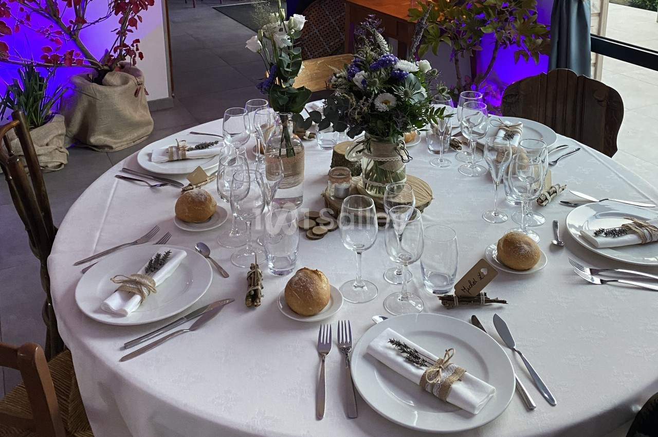 Table ronde dressée pour un repas, décorée avec des fleurs, des bougies et des serviettes ornées de brins de lavande.