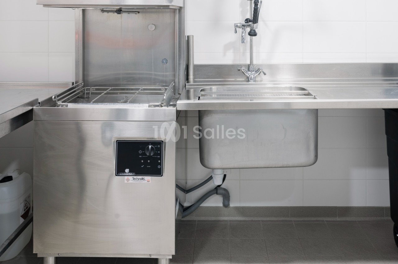 Lave-vaisselle professionnel en acier inoxydable à côté d'un évier dans une cuisine équipée.