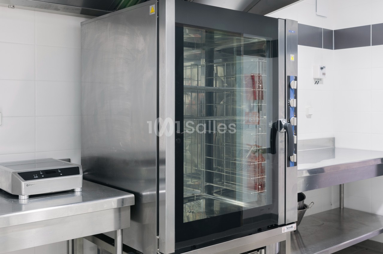 Four professionnel en acier inoxydable dans une cuisine équipée, avec balance électronique sur un plan de travail adjacent.