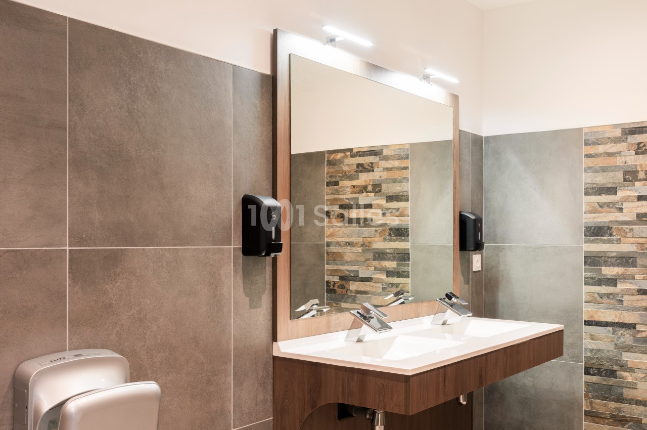 Lavabo double moderne avec robinetterie chromée, miroir éclairé et murs en carrelage gris et pierre décorative.
