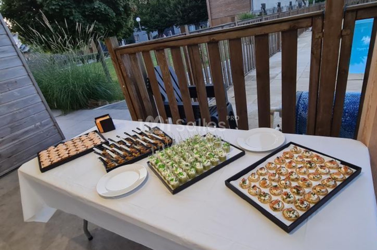 Plateau de canapés variés disposés sur une table blanche en extérieur, près d'une piscine et d'une clôture en bois.