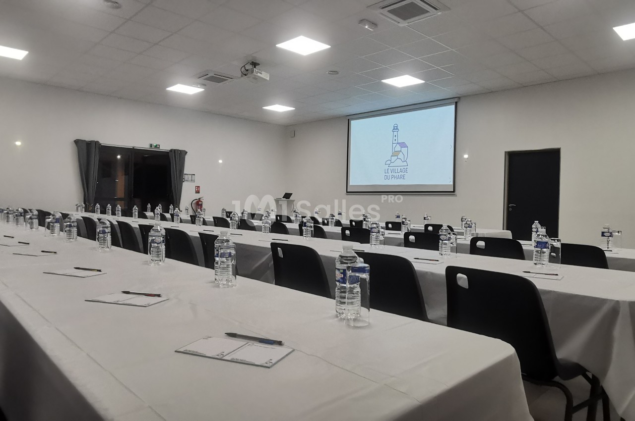 Salle de conférence aménagée avec des tables alignées, des bouteilles d'eau, des blocs-notes et un écran de projection…