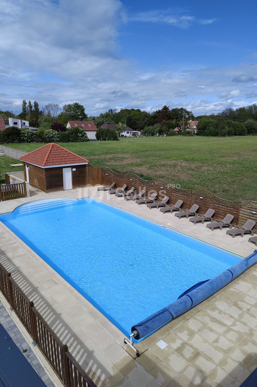 Piscine extérieure rectangulaire entourée de transats, avec un abri en bois et un paysage verdoyant en arrière-plan.