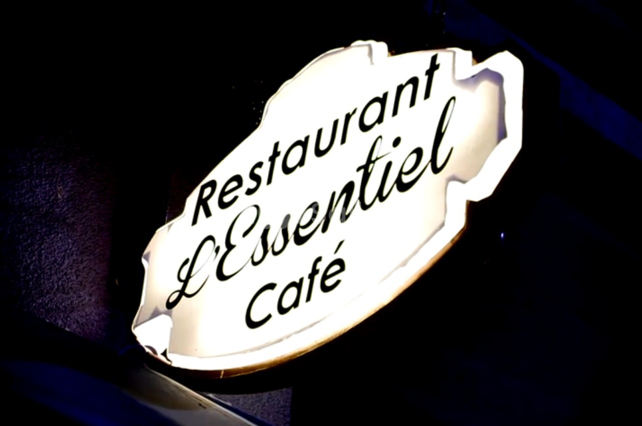 Enseigne lumineuse indiquant ’Restaurant L'Essentiel Café’ sur une façade sombre.
