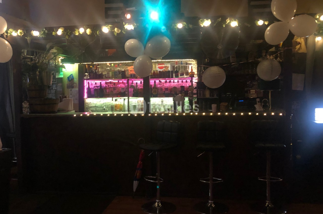 Bar décoré avec des guirlandes lumineuses, des ballons blancs et un éclairage coloré au-dessus du comptoir.