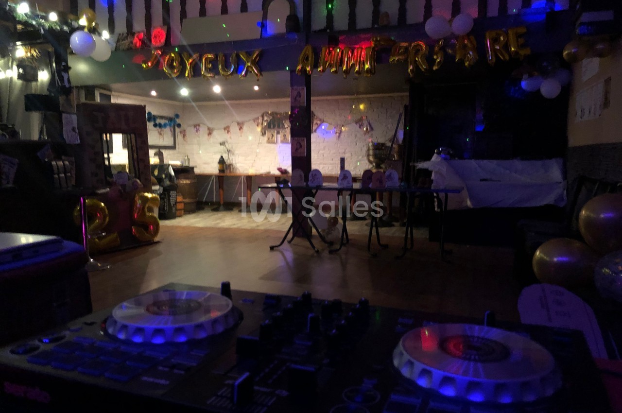 Salle décorée pour un anniversaire avec ballons, guirlandes lumineuses et une table de mixage au premier plan.