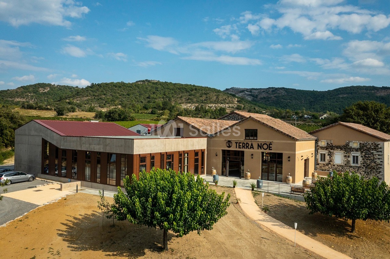 Vue aérienne d'un bâtiment moderne et traditionnel entouré de végétation et de collines sous un ciel dégagé.