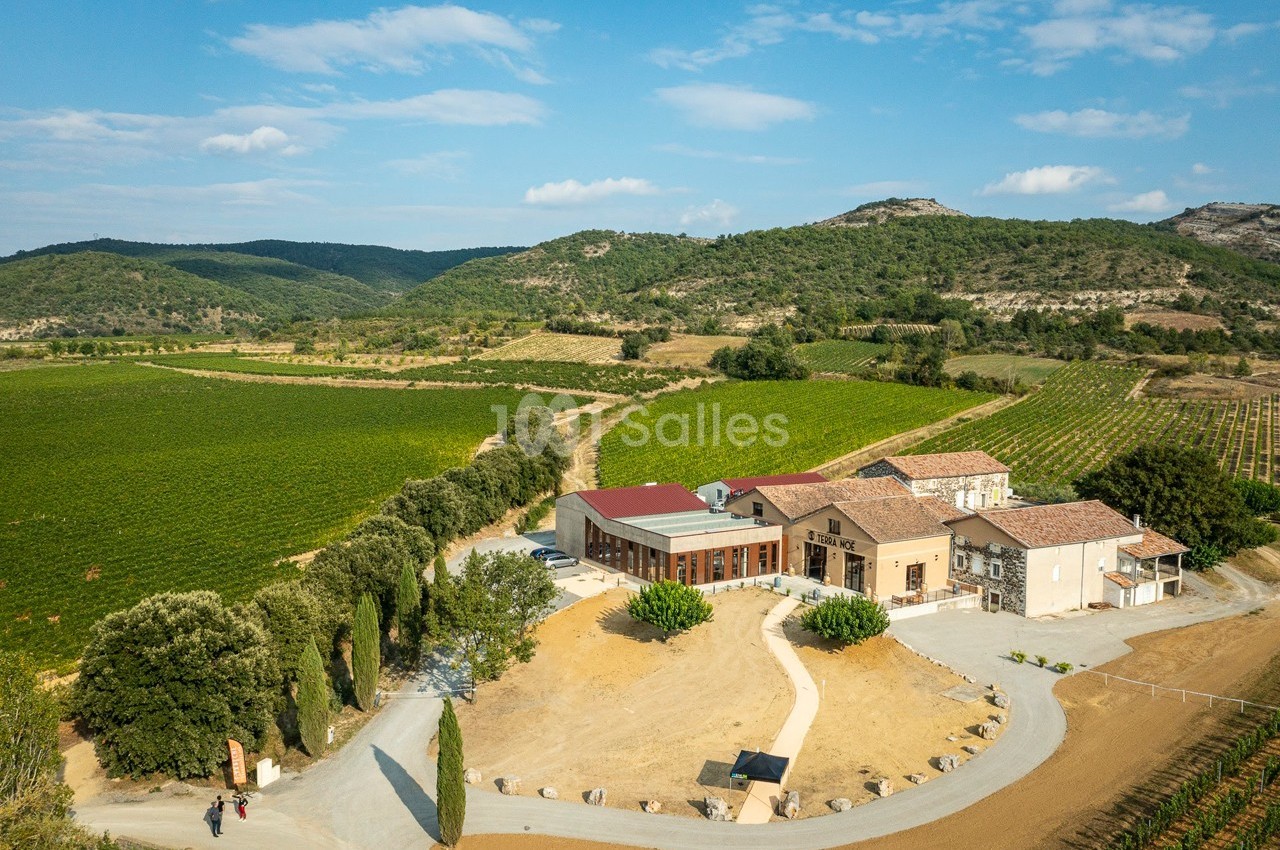 Vue aérienne d'un domaine viticole entouré de vignes et de collines sous un ciel partiellement nuageux.