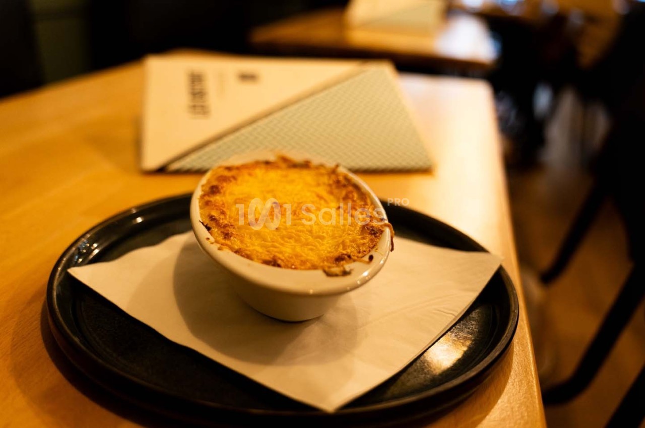 Gratin doré servi dans un petit plat blanc sur une assiette noire avec une serviette, posé sur une table en bois.