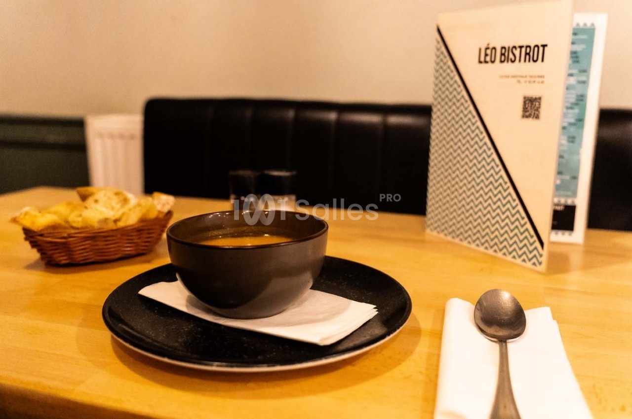 Bol de soupe sur une table en bois avec une corbeille de pain, une serviette et une carte de restaurant en arrière-plan.