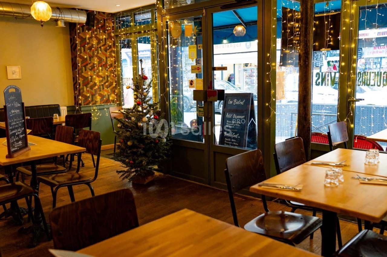 Salle de restaurant décorée pour Noël avec un petit sapin, des guirlandes lumineuses et des tables en bois dressées.