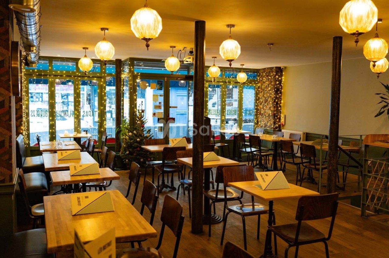 Salle de restaurant chaleureuse avec tables en bois, chaises disposées, éclairage doux et décorations lumineuses.