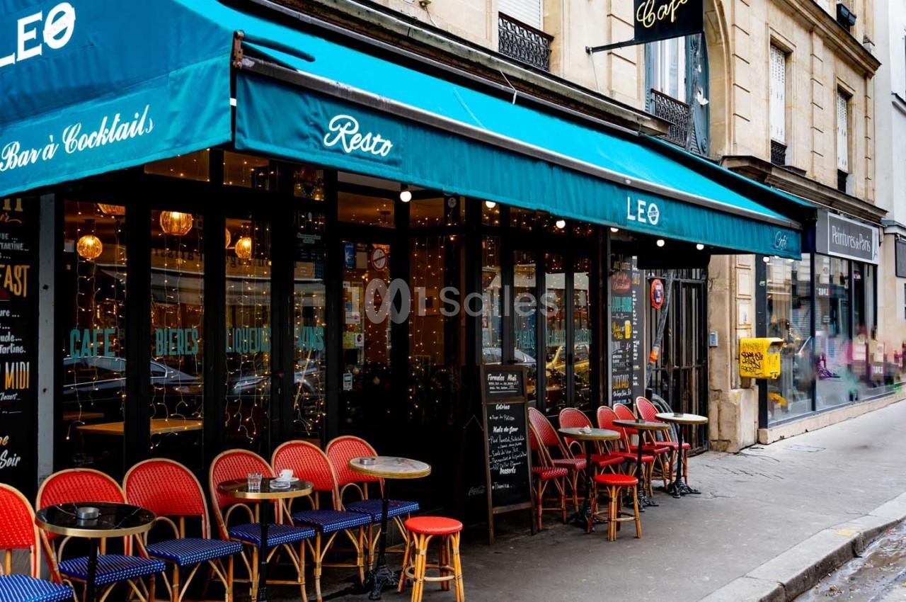 Façade d'un café-restaurant avec terrasse colorée et tables en extérieur, situé dans une rue urbaine animée.