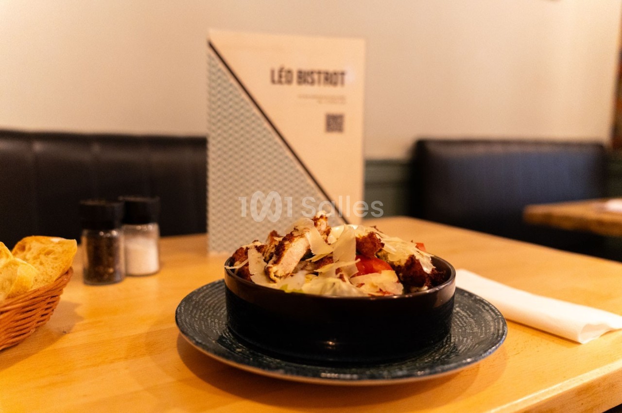 Bol de salade garnie de morceaux de poulet croustillant, posé sur une table en bois dans un restaurant.
