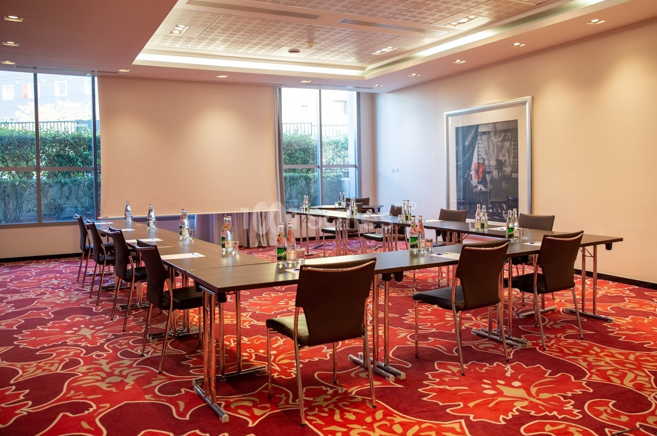 Salle de réunion lumineuse avec tables disposées en U, chaises en cuir, bouteilles d'eau et grandes fenêtres donnant sur l…