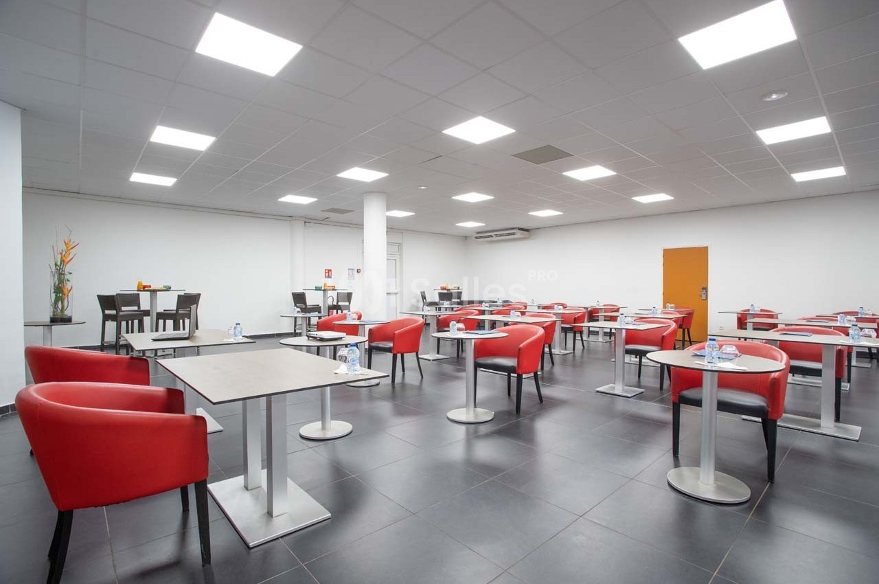 Salle de restauration moderne avec tables espacées, chaises rouges et éclairage au plafond.