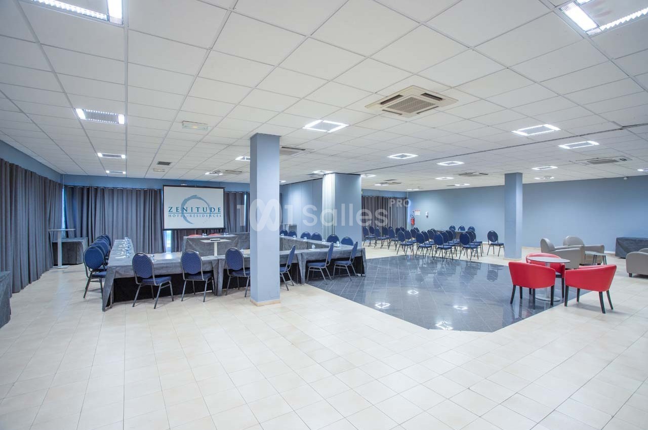 Salle de réunion spacieuse avec tables, chaises et éclairage lumineux, adaptée pour événements ou conférences.
