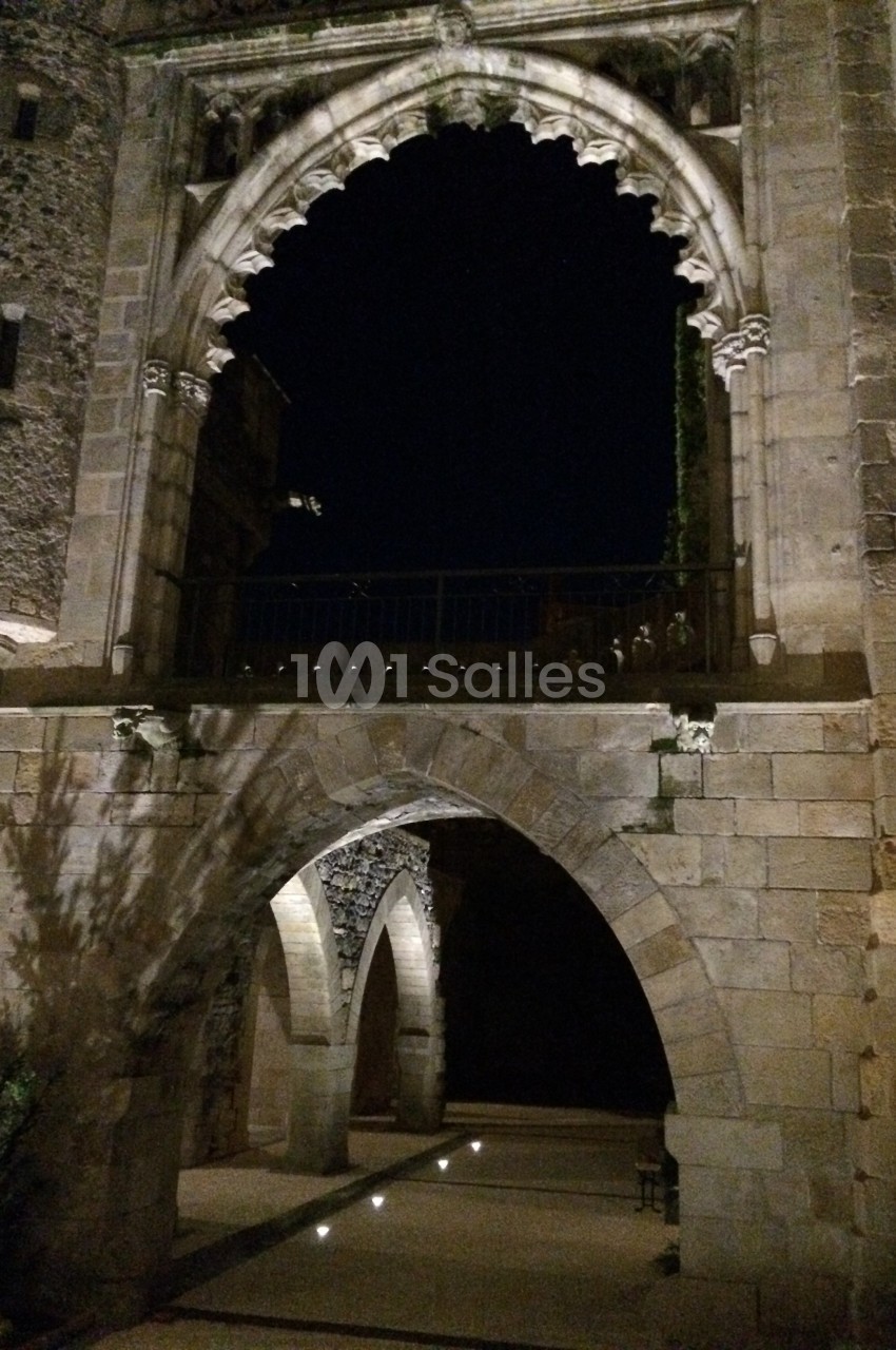 Arc gothique éclairé de nuit, encadrant un passage voûté en pierre dans un cadre architectural ancien.