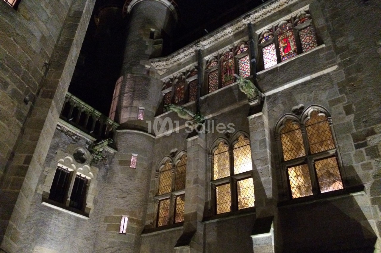 Façade d'un bâtiment ancien en pierre avec des fenêtres illuminées et des vitraux, vue de nuit.