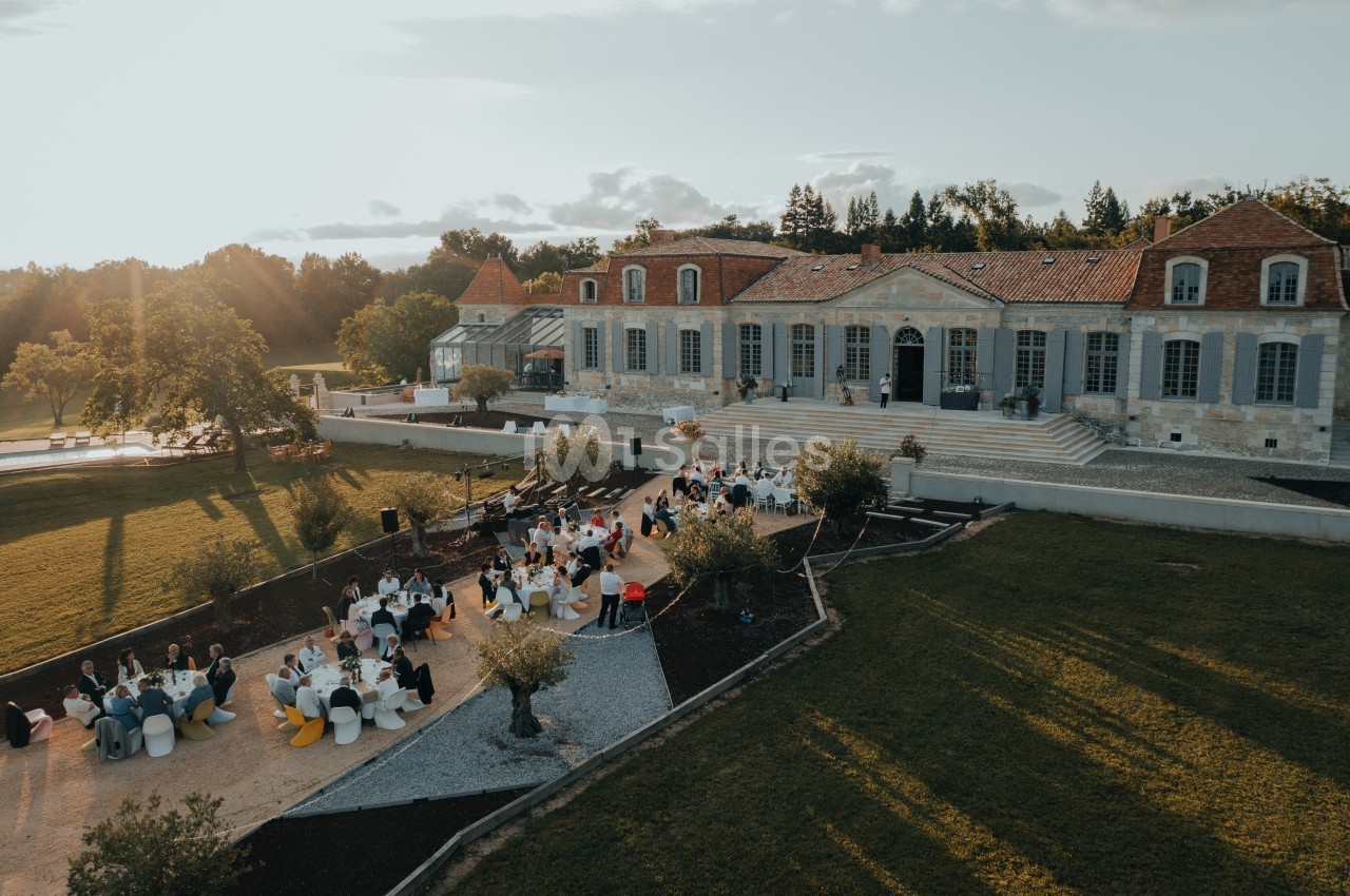 Vue aérienne d'un domaine avec une grande bâtisse en pierre et des invités assis à des tables en extérieur.