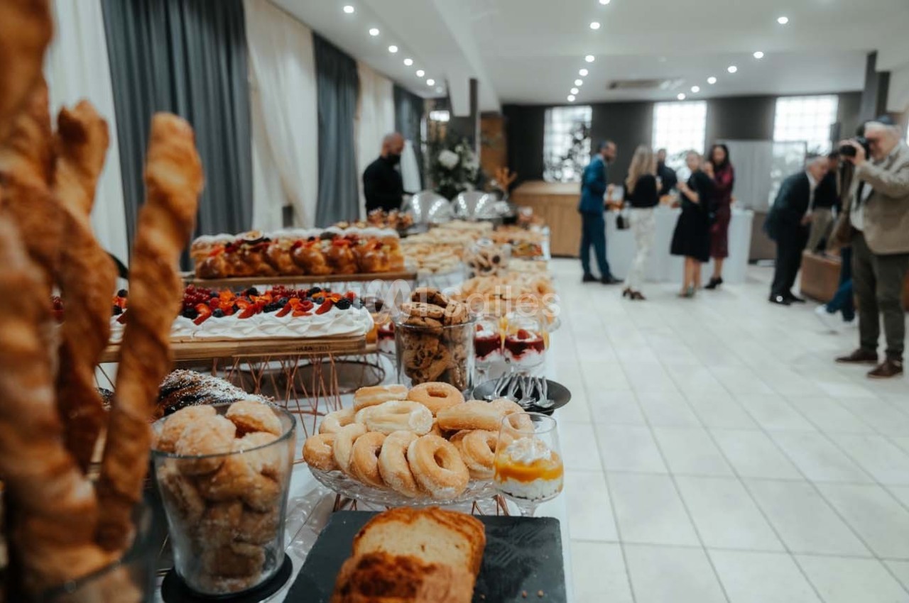 Buffet de pâtisseries variées disposées sur des tables dans une salle lumineuse avec des invités en arrière-plan.