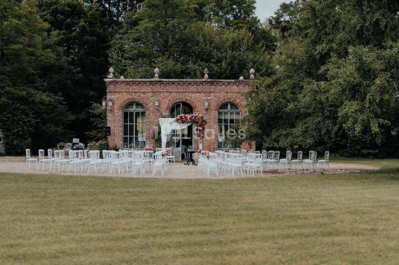 Chaises blanches disposées en extérieur devant un bâtiment en briques, décoré pour une cérémonie.