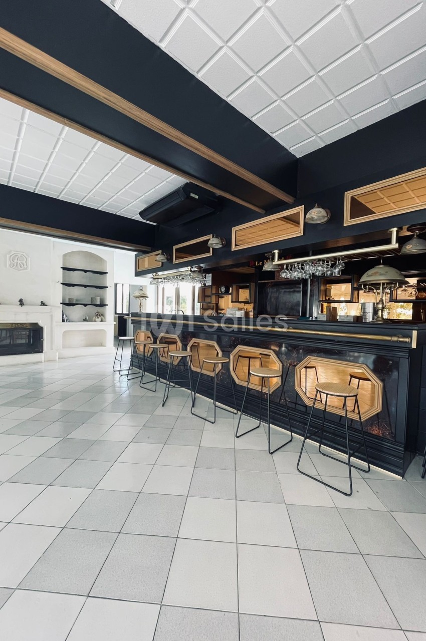Intérieur d'un bar moderne avec comptoir en bois, tabourets hauts, étagères et cheminée en arrière-plan.