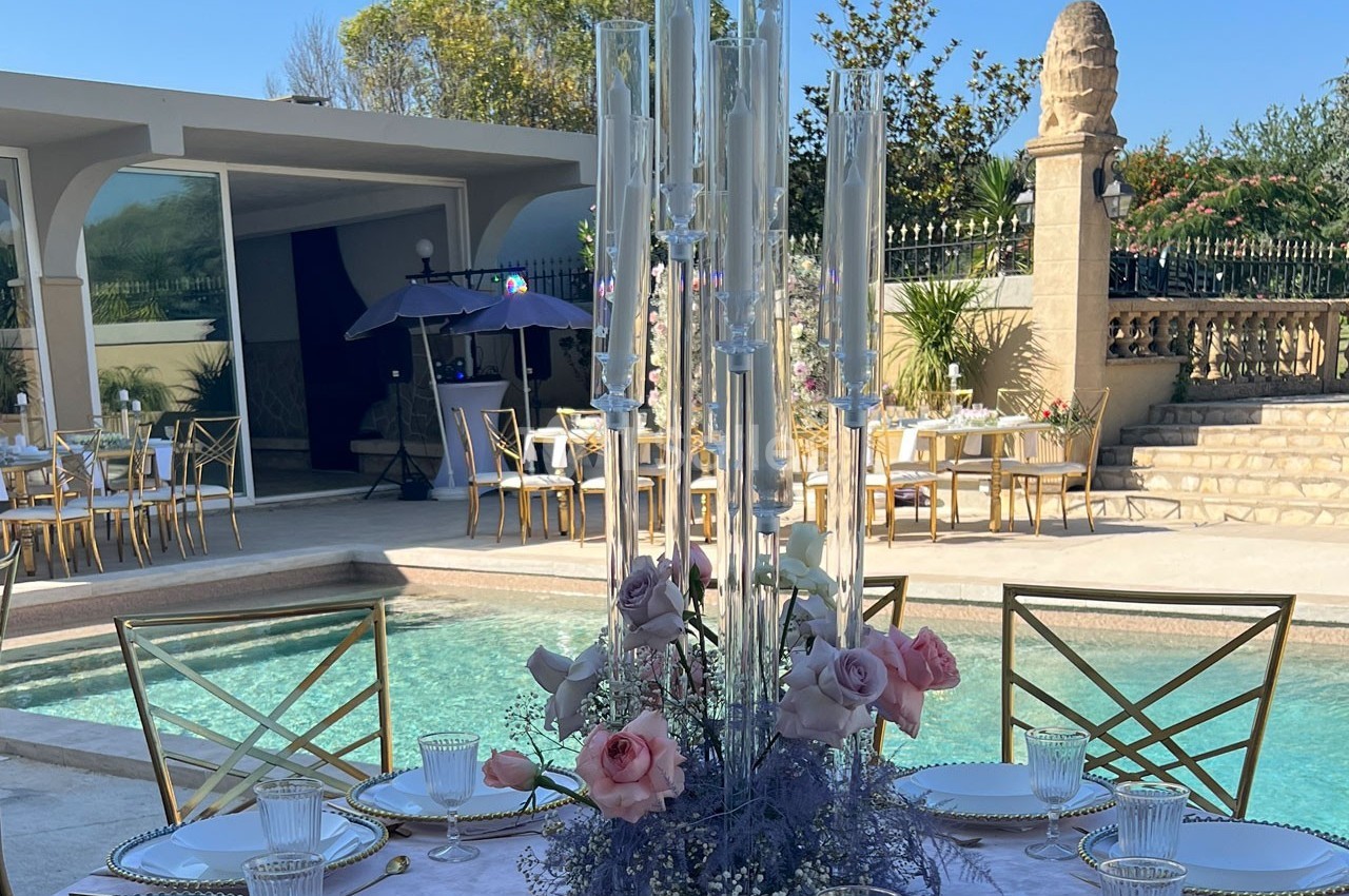 Centre de table floral avec roses et bougies, disposé près d'une piscine dans un cadre extérieur élégant.