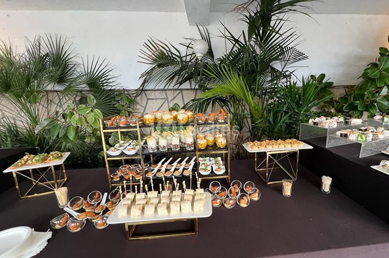 Buffet de réception avec divers amuse-bouches, verrines et sandwichs présentés sur des supports élégants, entourés de…