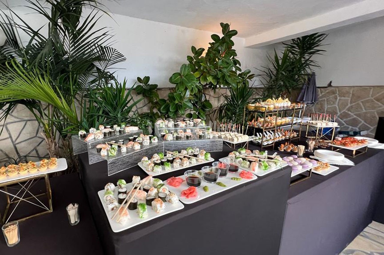 Buffet de sushis et amuse-bouches variés disposés sur des tables noires, entouré de plantes décoratives.