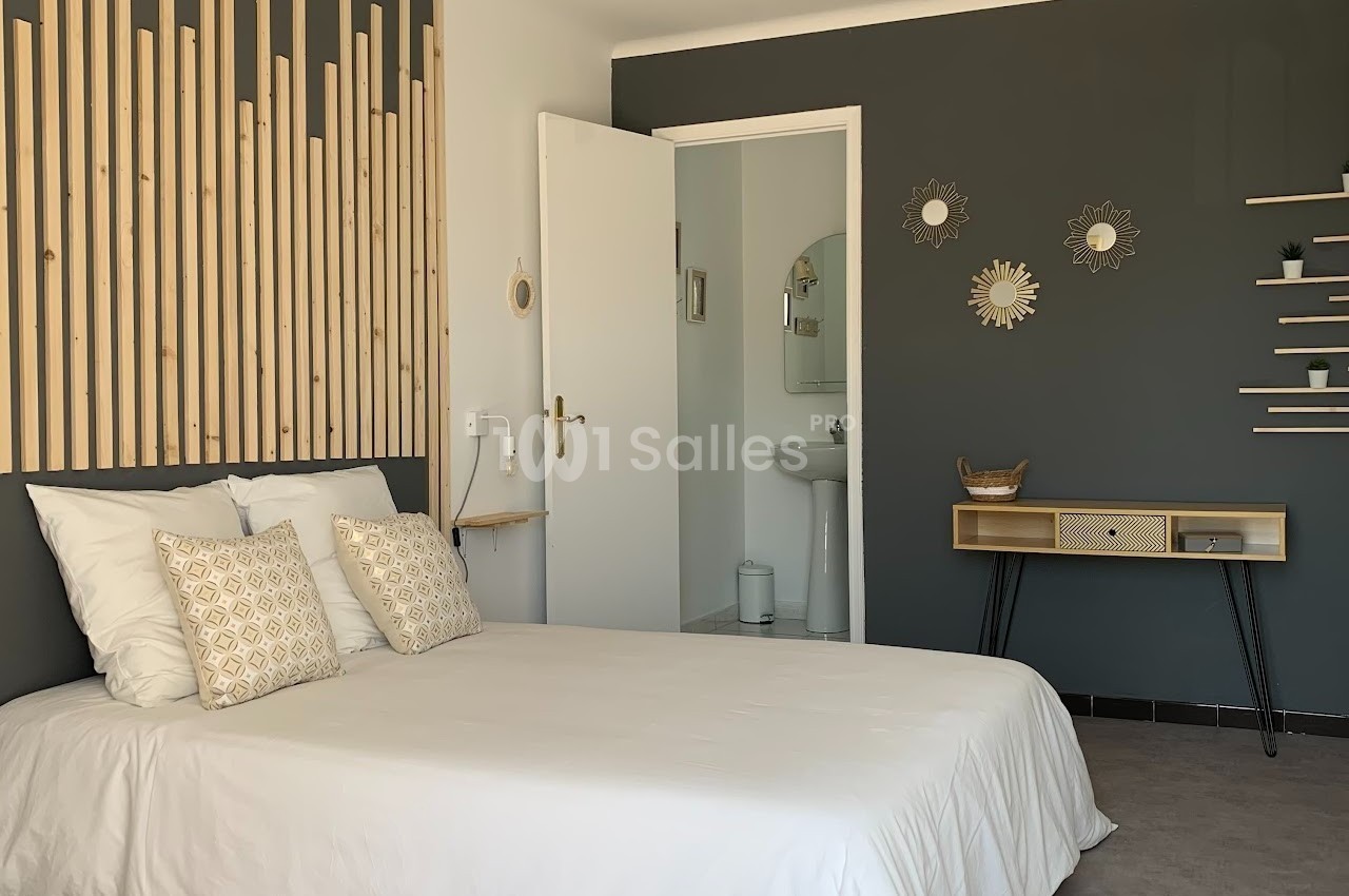 Chambre lumineuse avec lit double, décoration murale en bois et accès à une salle de bain attenante.