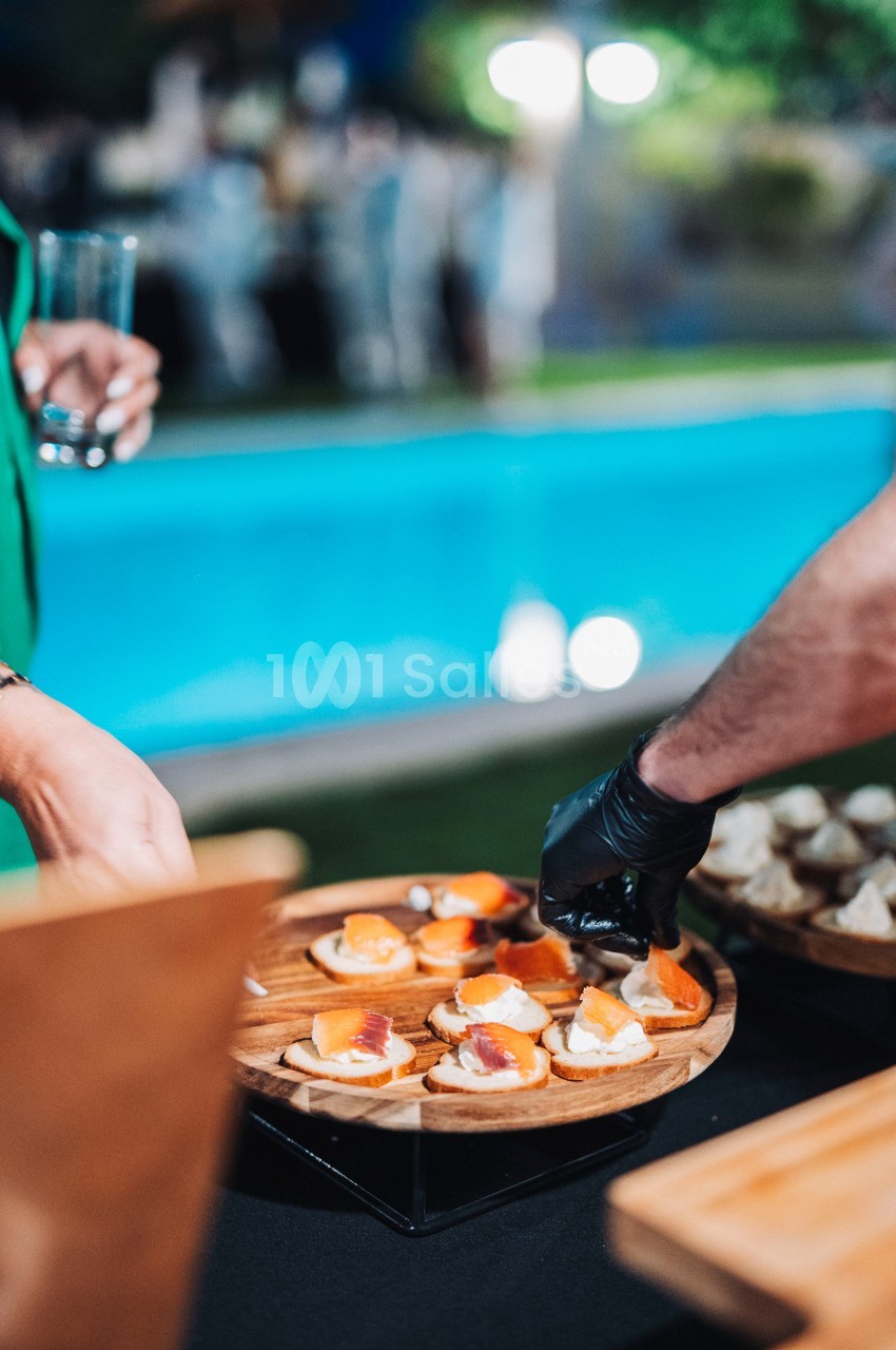 Plateau de canapés servis lors d'un événement en extérieur près d'une piscine, avec une main gantée les disposant.