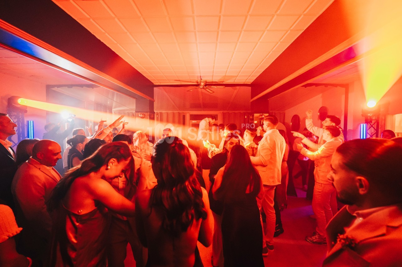 Groupe de personnes dansant dans une salle éclairée par des lumières rouges et oranges, ambiance festive.