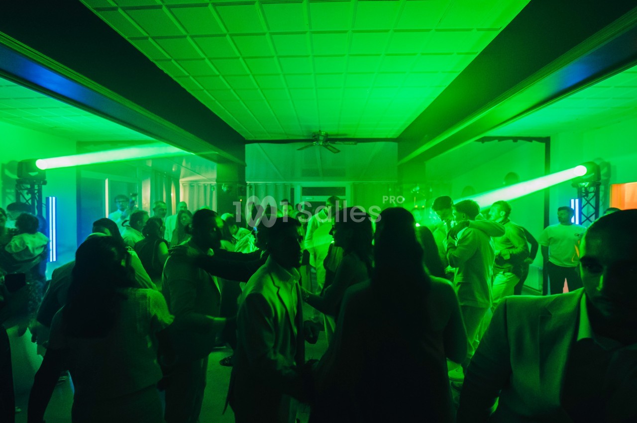 Personnes dansant dans une salle éclairée par des lumières vertes, ambiance festive et animée.