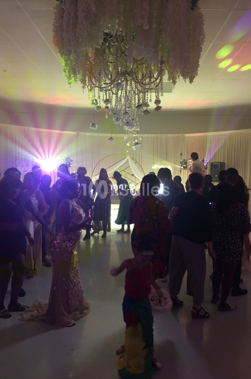 Groupe de personnes dans une salle de réception décorée, éclairée par des lumières colorées, lors d'un événement festif.